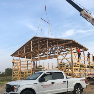 Wooden truss construction of large structure with a white truck sitting in the foreground